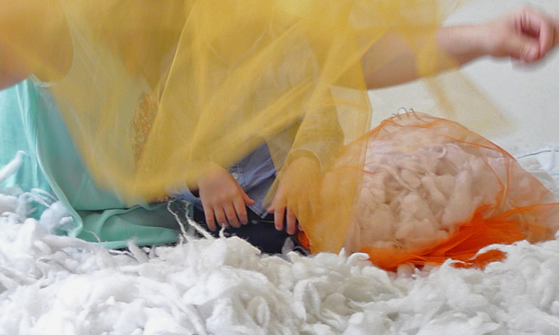 Transparent yellow material and chidren's hands behind. White furry material on the floor.